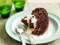 a piece of cake with icing on a plate next to a fork and two glasses