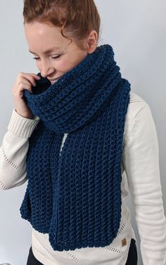 a woman wearing a blue knitted scarf is talking on her cell phone while standing in front of a white wall