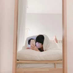 a person laying on a bed looking at a cell phone in front of a mirror