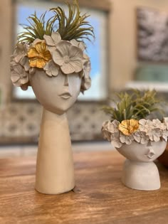 two vases with flowers and plants in them sitting on a wooden table next to each other