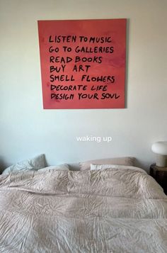 a bed with a pink sign on the wall above it that reads listen to music go to gallerys read books buy art smell decorate life design your soul