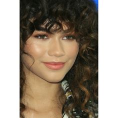 a close up of a person with long curly hair and blue eyeshadow smiling