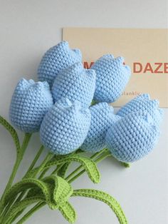 crocheted blue flowers are sitting on a white surface next to a business card