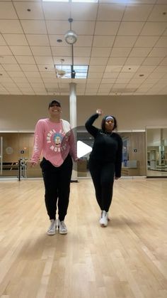 two women are dancing in an empty room with wooden floors and ceiling lights on the walls