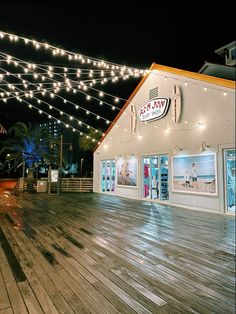 an empty boardwalk in front of a building with lights strung over it and people walking on the sidewalk