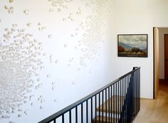 a stair case next to a white wall with flowers on it and a painting hanging on the wall