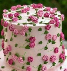 a white cake with pink roses on it sitting on a wooden table next to some green leaves