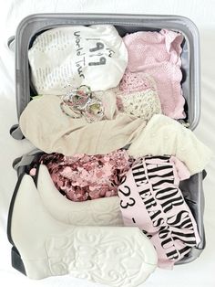 an open suitcase filled with clothes and other items on a white sheeted surface,