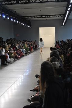 a woman is walking down the runway in front of a group of people watching her