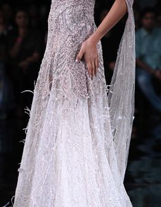 a woman in a white dress walking down the runway with her hand on her hip