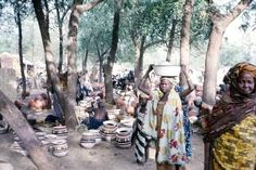 two women carrying pots on their heads in a forest with many people standing around them