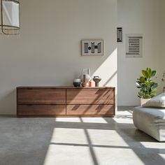 a living room with white walls and large wooden dresser in the center, surrounded by potted plants