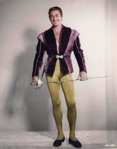 a man in yellow tights and a purple jacket holding a white object with one hand