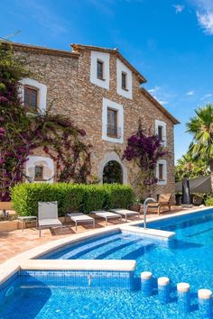 an outdoor swimming pool next to a stone building with white shutters on the windows