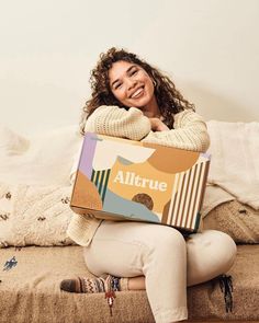 a woman sitting on a couch holding a box with the word allure written on it