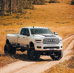 a white ram truck driving down a dirt road in the middle of a dry grass field