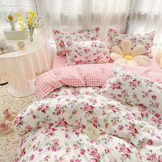 a bed with pink flowers and gingham sheets on it, in front of a window