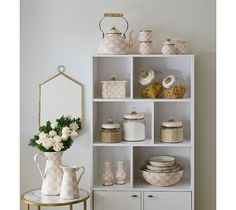 a white shelf filled with dishes and vases on top of each other next to a mirror