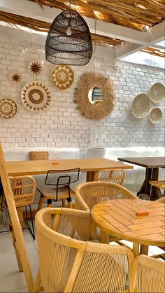 an outdoor dining area with wicker chairs and round wooden tables in front of a white brick wall