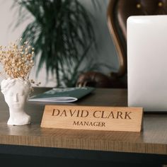 a desk with a wooden name plate on it and a laptop in the back ground