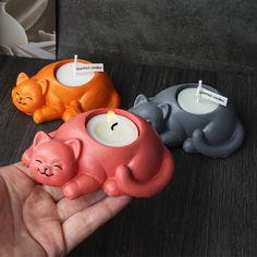 a hand is holding three candles in the shape of cats, one with a cat's head on it