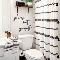 a white toilet sitting next to a sink in a bathroom under a shower curtain with writing on it