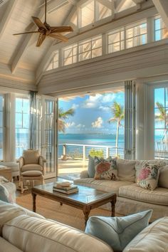 a living room filled with lots of furniture next to an ocean front window and ceiling fan