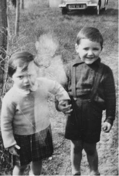 two young children standing next to each other in front of an old car and truck