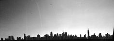 a black and white photo of a city with tall buildings in the distance, taken from an airplane window