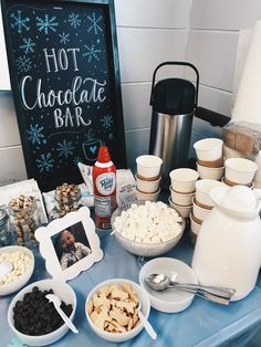 a blue table topped with bowls and plates filled with food next to a sign that says hot chocolate bar