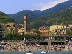 people are swimming in the water near some buildings and hills with mountains behind them,