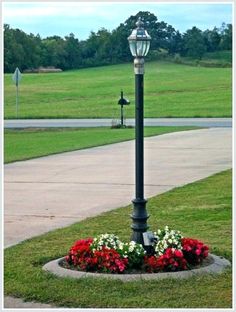 a lamp post with flowers around it in the middle of a sidewalk and grass area