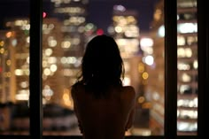 a woman standing in front of a window looking out at the night cityscape