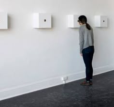 a woman is standing in front of three white boxes on the wall and looking at them