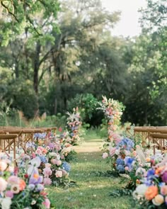 an outdoor ceremony with wooden chairs and flowers on the aisle, in front of trees