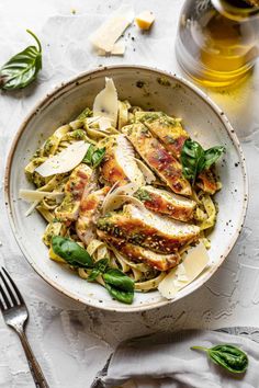 a white bowl filled with pasta and chicken on top of a table next to a glass of wine