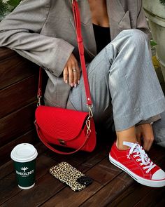 a woman sitting on a bench holding a red handbag and a cup of coffee