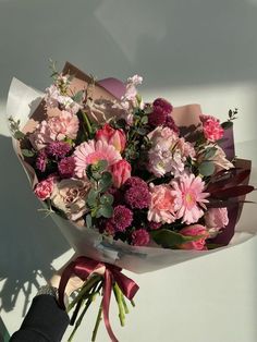 a bouquet of pink and white flowers is held by someone's hand on a sunny day