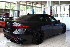 two cars are parked in a showroom, one is black and the other is red