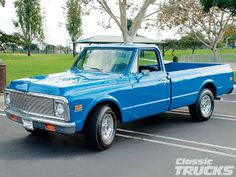 a blue pickup truck parked in a parking lot next to a tree and grass area