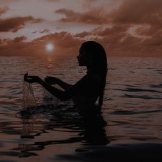 a woman sitting in the water holding a plastic bag with her hand and looking at the sky