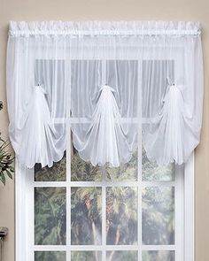 a white window with sheer curtains hanging from it's sides and two plants on the side