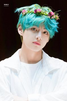 a man with blue hair wearing a white shirt and flowers in his hair is looking at the camera