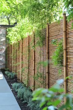 a long wooden fence is lined with plants and shrubs, along with a sidewalk in the foreground