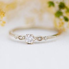 a white diamond ring sitting on top of a table next to flowers and greenery