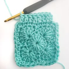 the crochet square is being worked on with a knitting needle in front of it