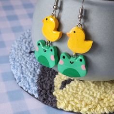 two yellow rubber ducks are hanging from green alligator earrings on a blue and white checkered tablecloth