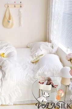 a bedroom with white bedding and flowers on the side table in front of it