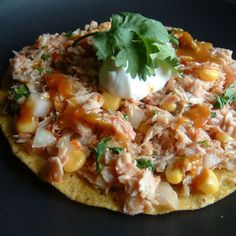 a tortilla topped with meat, vegetables and sour cream on a black plate