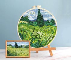 a cross - stitch picture is shown next to an easel with a painting on it